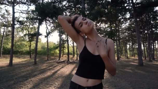 Joven chica punk bonita en cuello y paño negro con pelo rosa caminando en el bosque de pinos al atardecer — Vídeo de stock