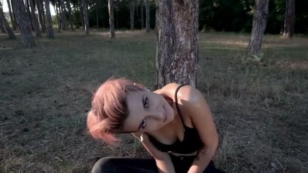 Fiatal csinos áttört lány a gallér és a fekete ruha ül a fa fenyő erdő alatt napnyugta időpontja — Stock videók