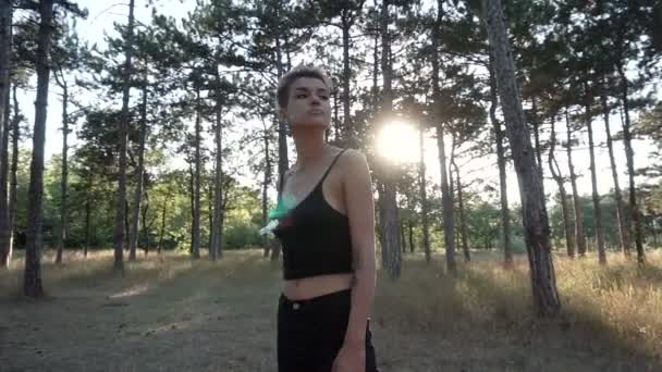 Giovane bella ragazza punk in colletto e panno nero con capelli rosa che camminano nella foresta di pini al tramonto — Video Stock