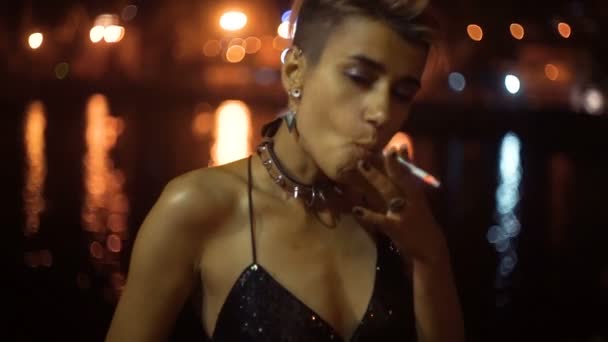 Street punk lub hipster dziewczyna z różowy włosów farbowanych. Kobieta z piercing w nosie, w uszach tunele i niezwykłe fryzury pali się na noc oświetlony miasto. — Wideo stockowe