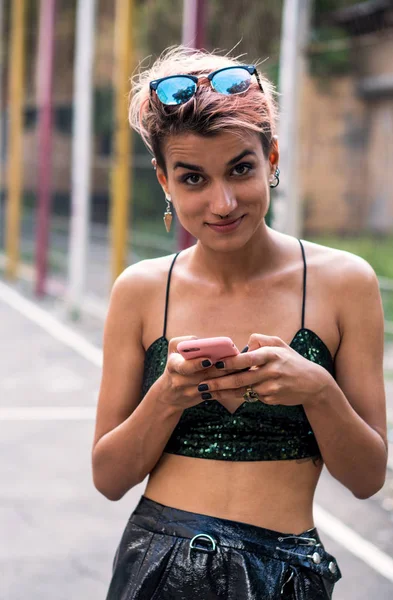 Kız pembe smartphone ile. Sokak serseri veya hippi kız pembe boyalı saçlı. Burun, kulaklar tünel ve duvarlarda grafiti boya ile basketbol sahası, sıradışı saç modeli piercing ile kadın — Stok fotoğraf