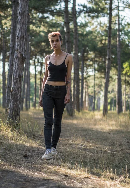 Junges hübsches Punk-Mädchen in schwarzem Tuch mit rosa Haaren im Kiefernwald bei Sonnenuntergang — Stockfoto