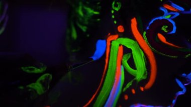 Bodyart ultraviyole ressam yüzünde güzel genç seksi kız yakın çizer