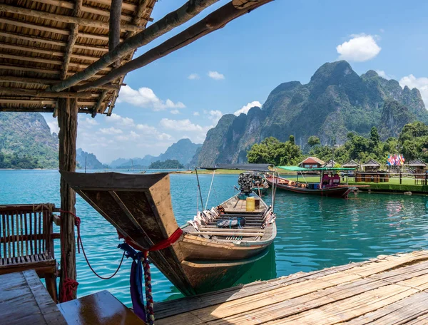 Wooden Thai traditional long-tail boat and floating wooden houses on a lake with mountains and rain forest in the background during a sunny day at Ratchaprapha Dam at Khao Sok National Park, Thailand — Stock Photo, Image