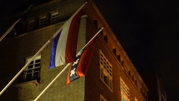 Banderas colgantes de los Países Bajos y de la ciudad de Amsterdam con tres cruces en la calle Night Street en Holanda después de la lluvia — Vídeos de Stock