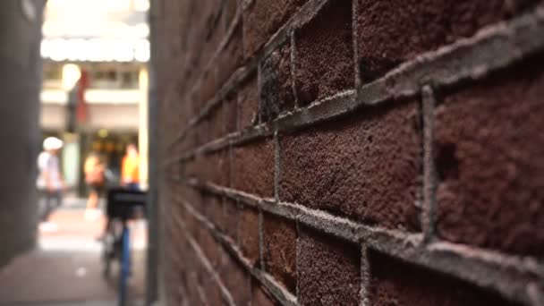 Tight Side Street Passage dans le centre d'Amsterdam, Pays-Bas. Mur de briques rouges et rue commerçante bondée en arrière-plan avec des personnes à pied et à vélo — Video