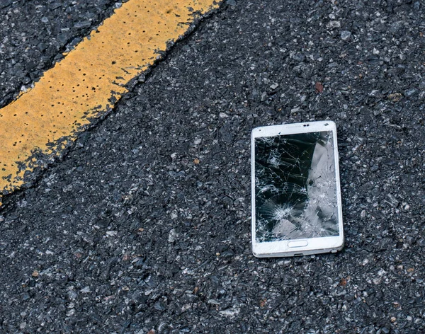 Novo Smartphone quebrado na estrada de asfalto. Alguém deixou cair o dispositivo. Rachaduras em uma grande exposição — Fotografia de Stock