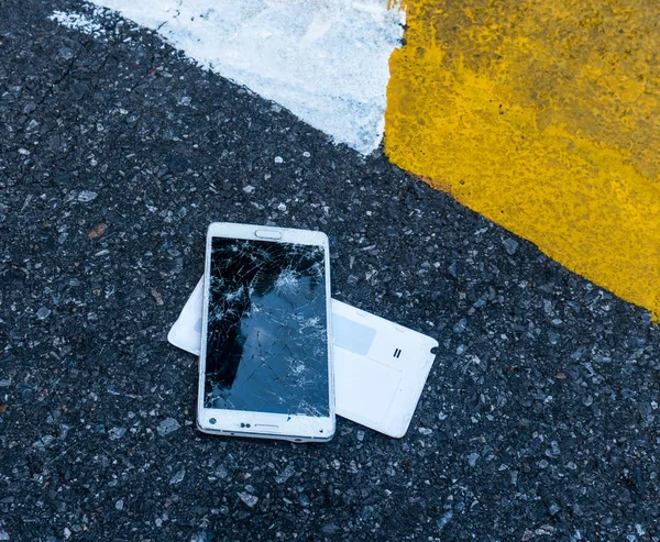 Novo Smartphone quebrado na estrada de asfalto. Alguém deixou cair o dispositivo. Rachaduras em uma grande exposição — Fotografia de Stock