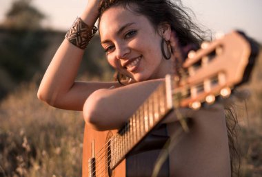 Gülümseyen çıplak kıvırcık esmer kız gitar alanında oturuyor