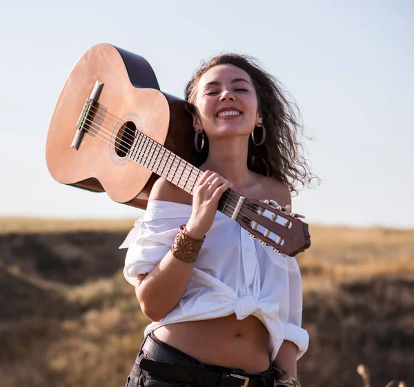 Esmer kız gitar bozkır tarafından yürüyüş alanı ile gülümseyen — Stok fotoğraf