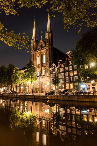 Catholic cathedral with Reflection in a Channel. Night city view of Amsterdam. Channel and typical dutch houses, Holland, Netherlands. — Stock Photo, Image