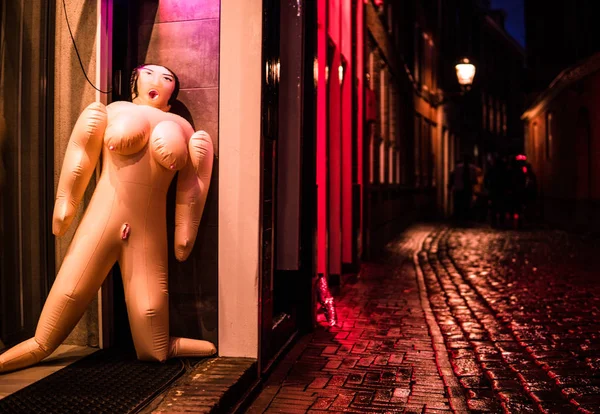 Red Light District in Amsterdam. Fake Sex Doll toy Lean to a wall on wet rainy street with Cobbles