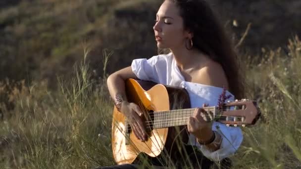 Lockiges, brünettes Zigeunermädchen, das auf dem Feld am Golfhang Gitarre spielt und singt — Stockvideo