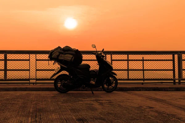 Silhouette de scooter sur le pont au coucher du soleil avec grand sac à dos de voyageurs sur le siège . — Photo