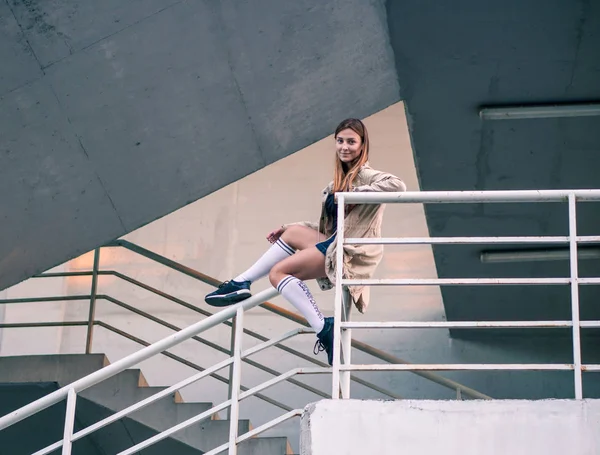 Utomhus hösten livsstil bild av en ung ganska kastanj haired kaukasiska flicka sitter och ler på gatan på trappan. Söt casual outfit framför byggnaden. — Stockfoto