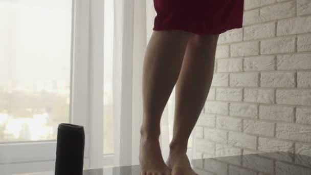 Une jolie fille brune dans une robe rouge essuyant un abat-jour de cuisine suspendu noir tout en se tenant debout sur une table pieds nus — Video