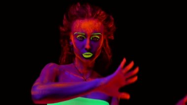 Vücudunda siyah ışıkta parlayan boya ile dans güzel bir genç seksi yarı çıplak kız. Siyah lamba ışığında parlayan bodyart güzel kadınla. Gülümseyen ve cagiran eller, sallayarak.