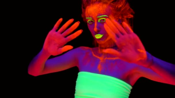 A beautiful young sexy half-naked girl crossing her hands and dancing with glowing paint on her body in black light. Pretty woman with glowing bodyart in black lamp light. — Stock Video