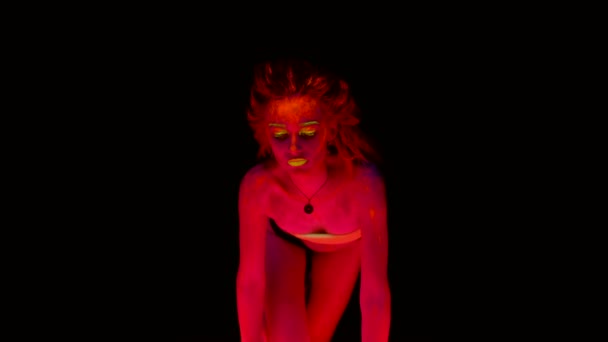 A beautiful young sexy half-naked standing kneeling on all fours with glowing paint on her body in black light looking provocative. Pretty woman with glowing bodyart in black lamp light. — Stock Video