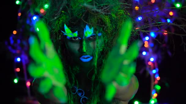 Мистик зеленый дриада чувствует магическую силу в ее пальцах в ультрафиолетовом флуоре черный свет с светящимися деревьями на заднем плане — стоковое видео
