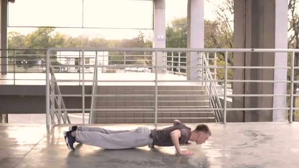 Молодой хулиган-уличный парень делает упражнения по кроссворду на открытом воздухе на лестнице входа на стадион. Спортивный стиль жизни — стоковое видео