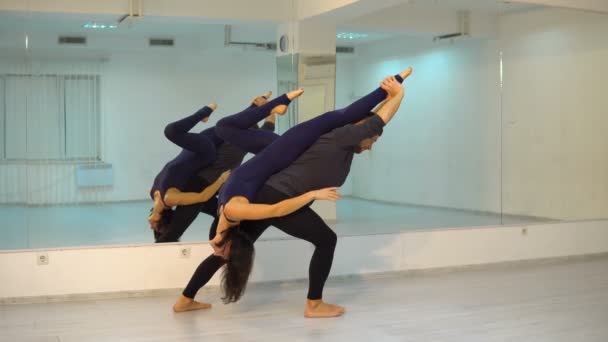 Young athletic couple in dark suits practicing acroyoga in studio with mirrors. Balancing in pair — Stock Video
