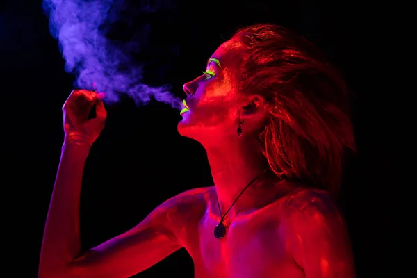 Portréja egy fiatal dohányzás szexi lány ultraibolya festék a testén. Szép nő, a fekete lámpa fény izzó bodyart — Stock Fotó