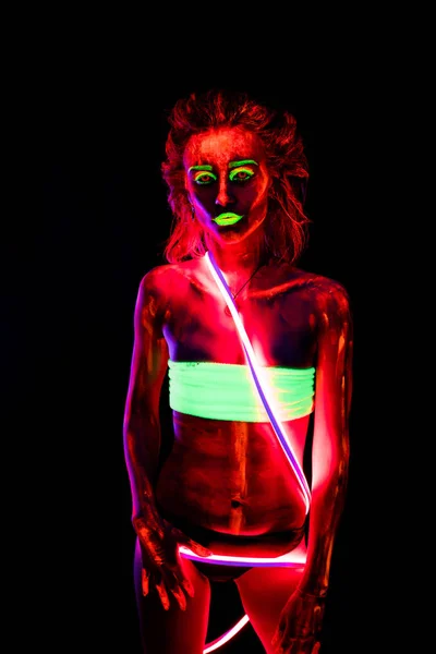 Porträtt av en vacker ung sexig flicka i neon lånade med ultraviolett färg på hennes kropp. Pretty woman med glödande bodyart i svart lampa ljus — Stockfoto