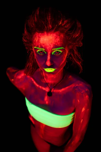 Porträtt av en vacker ung sexig flicka med ultraviolett färg på hennes kropp. Pretty woman med glödande bodyart i svart lampa ljus — Stockfoto