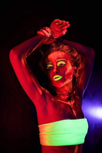 Porträtt av en vacker ung sexig flicka med ultraviolett färg på hennes kropp. Pretty woman med glödande bodyart i svart lampa ljus — Stockfoto