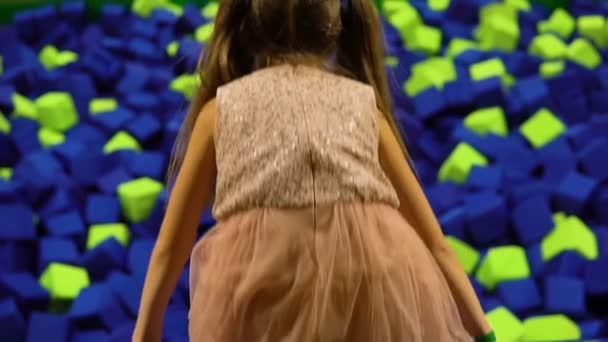 Маленька дівчинка стрибає в сухий басейн з м'якими кубиками. Дитяча планета — стокове відео