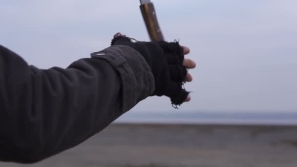 Mano de hombre en guantes hechos a mano sin dedos Arroja un machete grande y lo hace girar en Wasteland. Nublado clima oscuro, otoño invierno — Vídeos de Stock