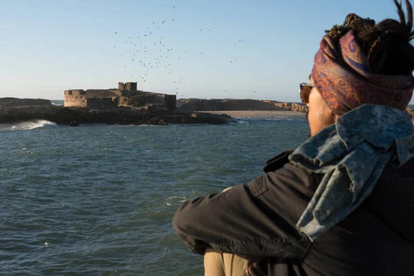 Jovem Asiático Barbudo Homem turístico com Dreadlocks e cachecol na cabeça Caminhando na costa do oceano em Essaouira, Marrocos, à noite, horário de pôr do sol — Fotografia de Stock
