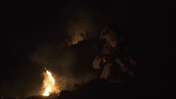 Stalker overlevende soldaat dragen gasmasker in een scenario apocalyps oorlog zittend met ouderwetse geweer en nemen doel in de buurt van het vuur — Stockvideo