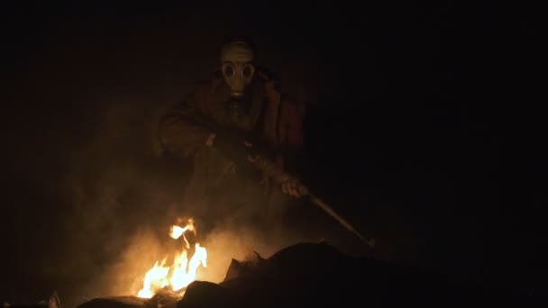 Выживший преследователь Солдат в противогазе в сценарии войны Апокалипсиса сидит со старомодной винтовкой и целится у огня — стоковое видео