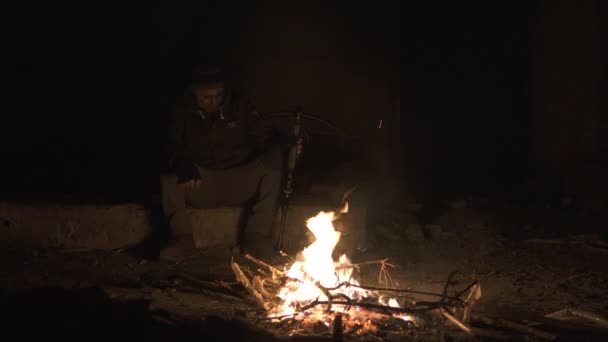 Çirkin tehlikeli zombi canavar karanlık yıkık beton barınak ağır Cross Bow ile şenlik ateşi yakınında oturuyor. Korku karakter kavramı, silahlı ve grasepainted varlık — Stok video