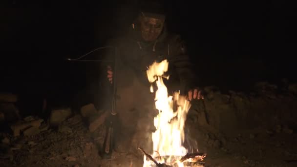 Άσχημο επικίνδυνο τέρας ζόμπι καθισμένος κοντά στην φωτιά με βαρύ σταυρό τόξο στο σκοτεινό κατέστρεψε τσιμεντένιο καταφύγιο. Αντίληψη του χαρακτήρα τρόμου, οπλισμένη και ζωγραφισμένη οντότητα — Αρχείο Βίντεο