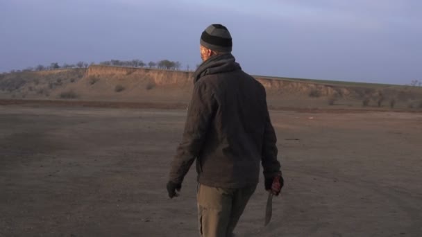 Ein gefährliches Zombie-Monster mit großer Machete läuft umher und sieht sich in der Wüste um. Horrorfigur postapokalyptisches Verfolgungskonzept, bewaffnet und greifbar — Stockvideo