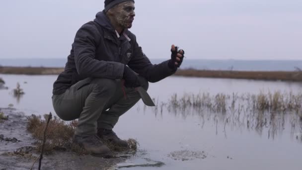 Un mostro mutamt arrabbiato con grande machete venire al fiume e gustare un'acqua in maleducato tempo nuvoloso. Concetto di personaggio dell'orrore, entità armata e dipinta ad erba — Video Stock