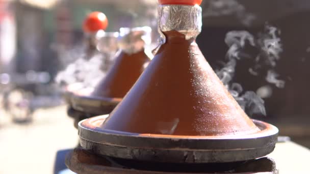 Cocina tradicional tajina marroquí en macetas tajinas al fuego con humo y tomates en la parte superior — Vídeo de stock