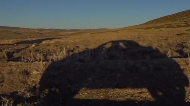 Ombre d'une voiture se déplaçant par la route de campagne dans le vaste paysage de friches à l'heure du coucher du soleil 