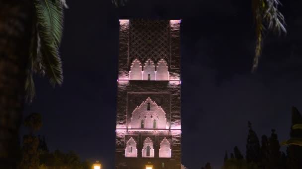 Ночной вид на башню Хассана с площади с фонарями и флагами в Рабате, Марокко. Незаконченный минарет мечети с видом на мавзолей короля Хассана II. Остатки самой большой старой цивилизации в Африке — стоковое видео