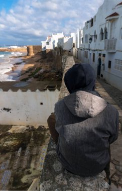 Landmark Asilah-Atlantik Okyanusu sörf ve deniz kenarı beyaz evler ile eski şehir duvarı. Adam Asilah duvarında oturan, Fas