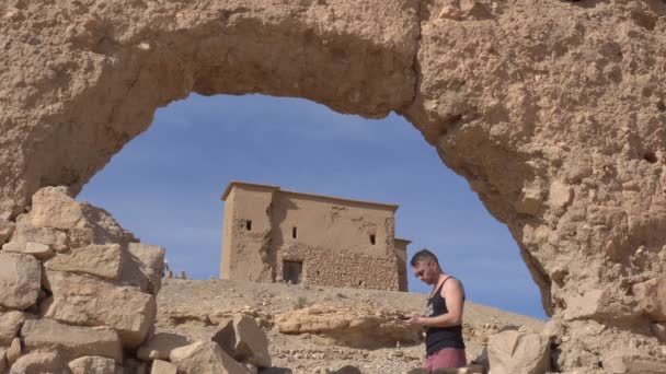 Traveler man menggunakan smartphone-nya untuk navigasi GPS di busur batu Ancient Remains di Maroko. Perjalanan di Ourzazate, Ait Benhaddou — Stok Video