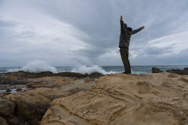 Ufukta uzak görünümlü deniz yakınındaki kayalar üzerinde gezgin. Rocky Atlantik Okyanusu kıyı şeridi ve fırtınayı hava. Doğa açık havada Casual kıyafetler yakışıklı genç Kafkas turist adam