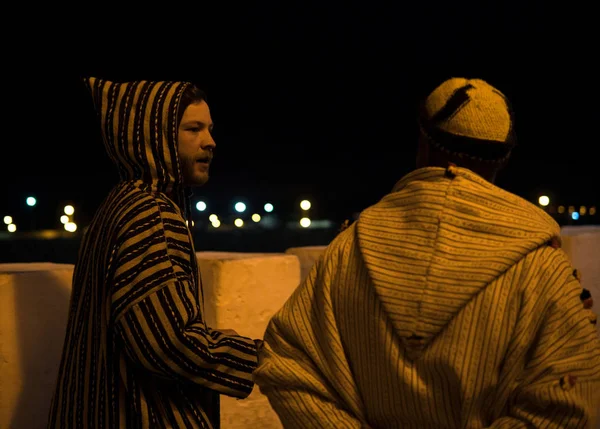 Two Man in Traditional moroccan djellaba walking on the street of Asilah Medina, on Atlantic Coast in Morocco. Caucasian with a local Moroccan man
