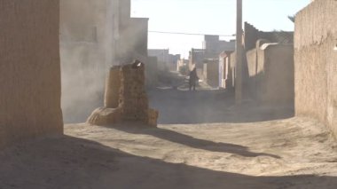 Fas, Afrika kil köyünde Street Shot Alley. Duman ve toz üstesinden gelmek için su hortumu kullanarak djellaba bir adam