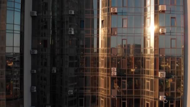 屋外のガラスのミロウ窓とモダンなデザインの超高層ビルの空中ショット。日没時に別の1つのガラスの高層ビルを反映した近代的なアパートの建物のガラスファサード — ストック動画