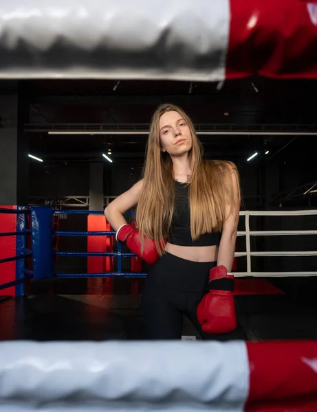 Blonde Caucasian fighter girl in Red Boxing Gloves is posing on Fight club boxing ring