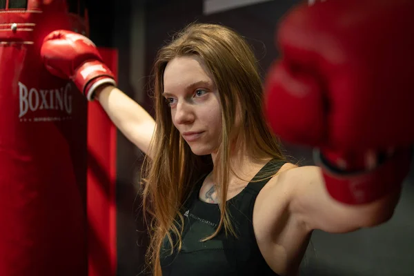 Blondes kaukasisches Kämpfermädchen in roten Boxhandschuhen posiert in der Trainingshalle des Kampfklubs — Stockfoto
